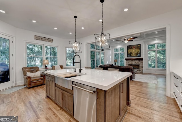 kitchen with white cabinetry, sink, a kitchen island with sink, stainless steel dishwasher, and a brick fireplace