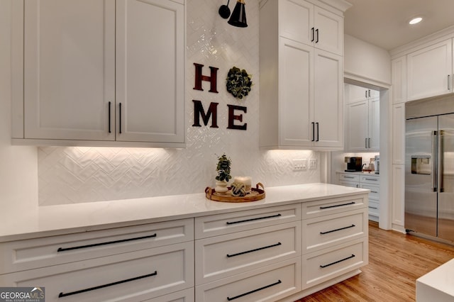 kitchen with built in refrigerator, tasteful backsplash, white cabinets, and light wood-type flooring