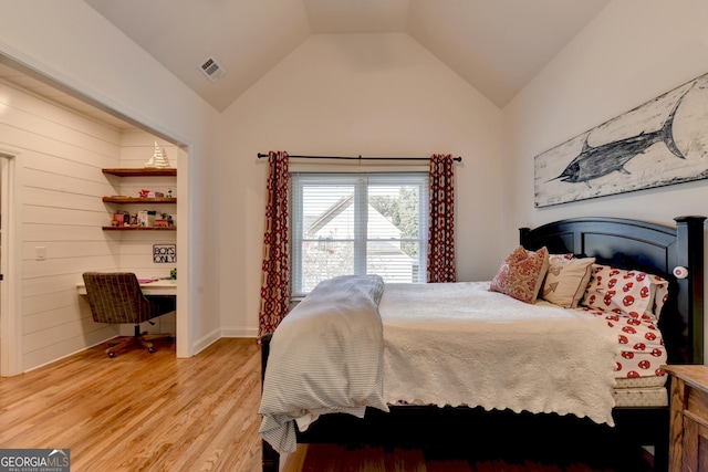 bedroom with built in desk, vaulted ceiling, and light hardwood / wood-style flooring