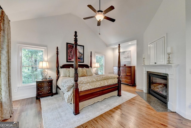 bedroom featuring ceiling fan, high vaulted ceiling, a high end fireplace, and light hardwood / wood-style floors