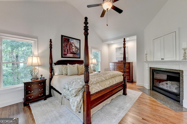 bedroom featuring light hardwood / wood-style flooring, a fireplace, vaulted ceiling, and ceiling fan