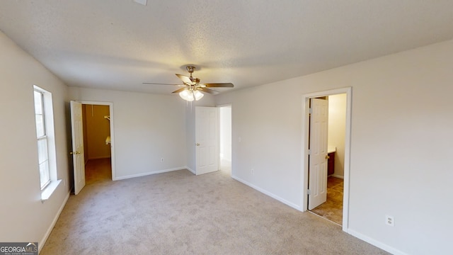 unfurnished bedroom featuring ensuite bathroom, a spacious closet, light colored carpet, ceiling fan, and a textured ceiling