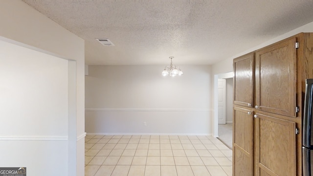 tiled spare room with a textured ceiling and a notable chandelier