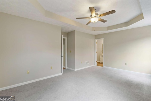 spare room with ceiling fan, light colored carpet, a tray ceiling, and a textured ceiling