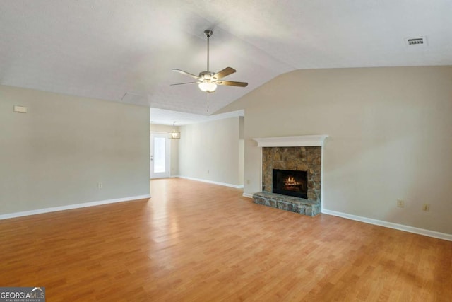 unfurnished living room with ceiling fan, lofted ceiling, a stone fireplace, and light hardwood / wood-style flooring