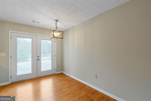 doorway with an inviting chandelier, hardwood / wood-style flooring, french doors, and a textured ceiling