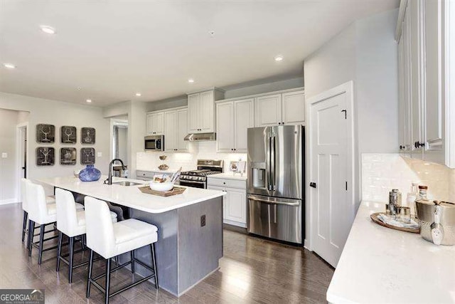 kitchen with sink, a breakfast bar area, appliances with stainless steel finishes, a kitchen island with sink, and white cabinets