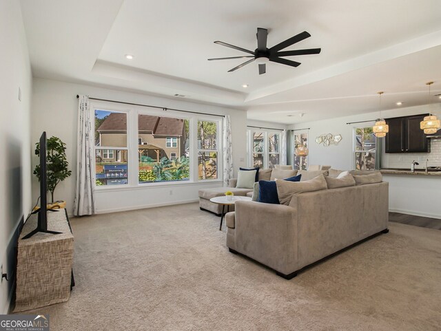 living room featuring light carpet, a tray ceiling, and ceiling fan