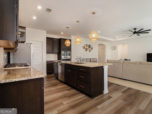 kitchen featuring appliances with stainless steel finishes, dark brown cabinets, a kitchen island with sink, and decorative light fixtures