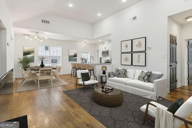 living room with hardwood / wood-style flooring, a high ceiling, sink, and a chandelier