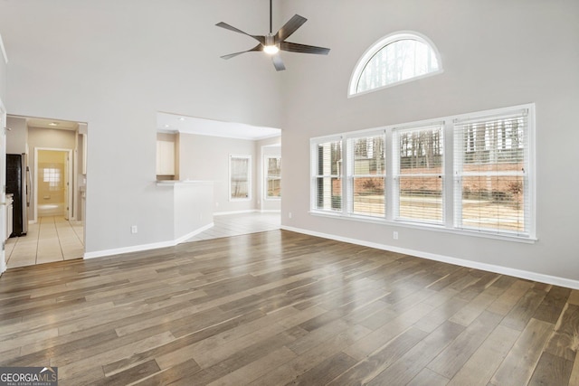 unfurnished living room featuring a high ceiling, wood-type flooring, and ceiling fan