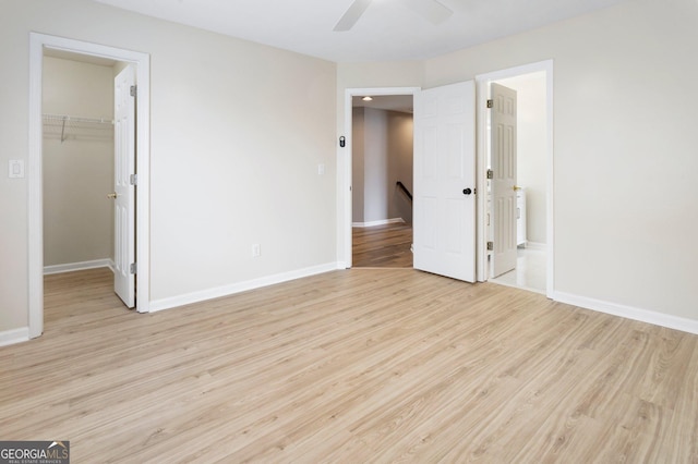 unfurnished bedroom with ensuite bathroom, a walk in closet, light wood-type flooring, a closet, and ceiling fan