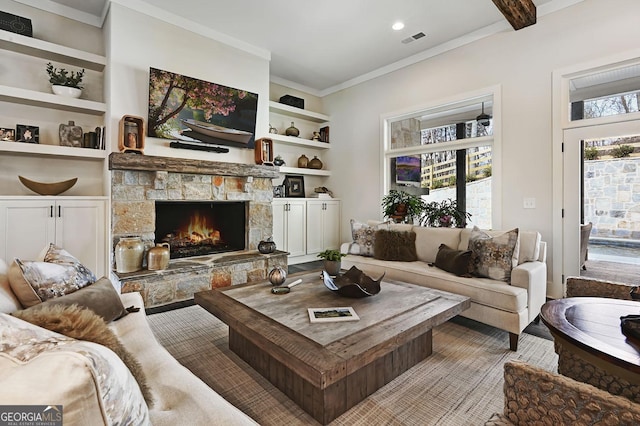 living room with built in shelves, crown molding, and a stone fireplace