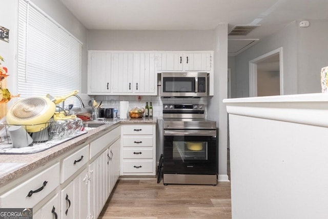 kitchen featuring white cabinetry, decorative backsplash, stainless steel appliances, and light hardwood / wood-style floors