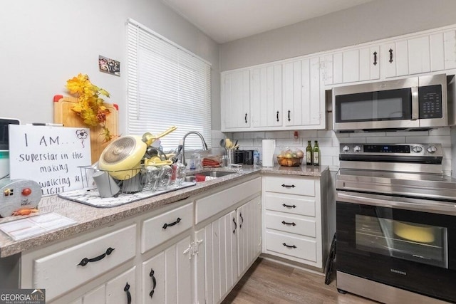 kitchen with sink, tasteful backsplash, wood-type flooring, oven, and white cabinets