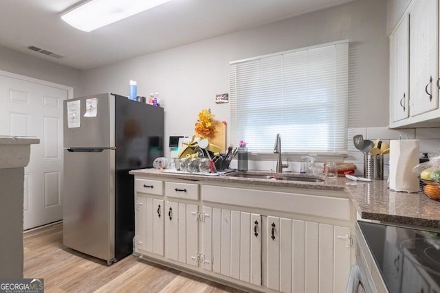 kitchen with sink, light hardwood / wood-style flooring, stainless steel appliances, white cabinets, and dark stone counters