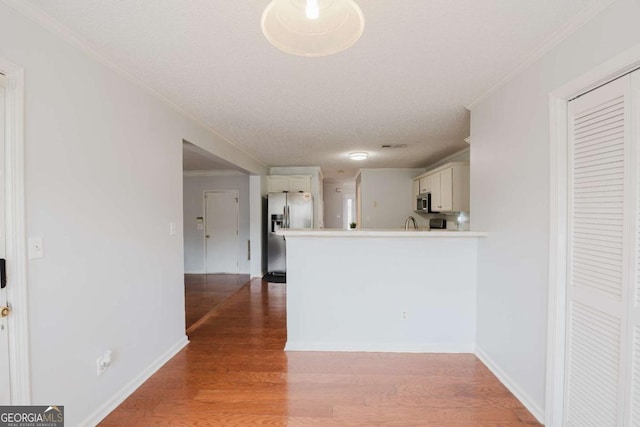 kitchen featuring hardwood / wood-style flooring, appliances with stainless steel finishes, white cabinets, and kitchen peninsula