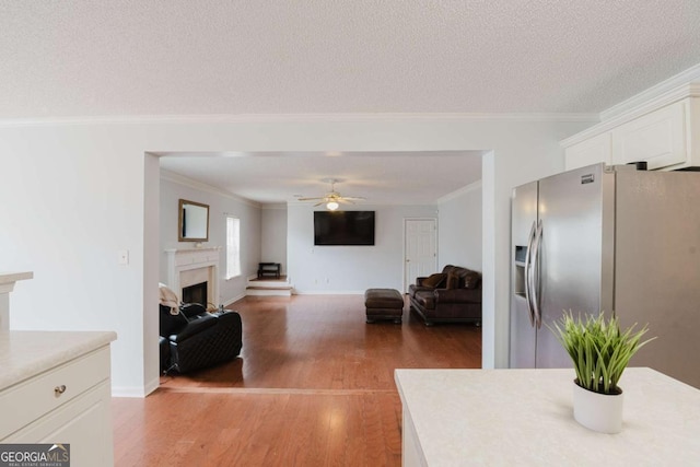 interior space with white cabinetry, crown molding, a textured ceiling, stainless steel fridge, and hardwood / wood-style floors