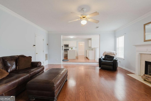 living room with wood-type flooring, ornamental molding, a premium fireplace, and ceiling fan