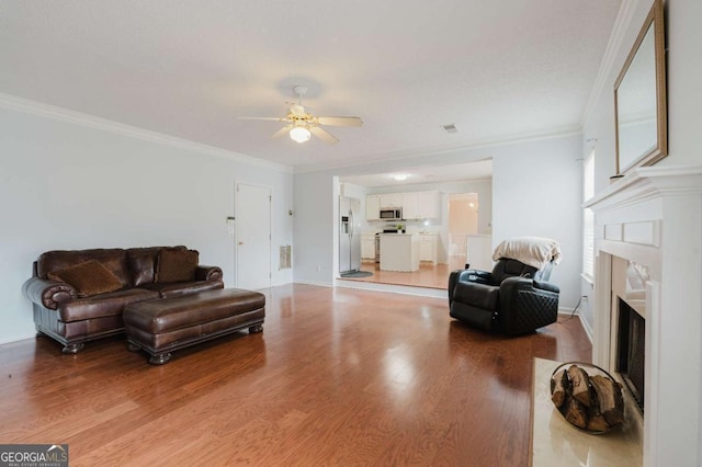 living room featuring wood-type flooring, ornamental molding, and ceiling fan