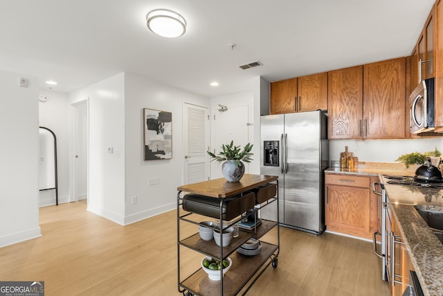 kitchen featuring appliances with stainless steel finishes, light hardwood / wood-style floors, and dark stone counters