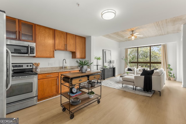 kitchen with sink, light wood-type flooring, ceiling fan, stainless steel appliances, and light stone countertops