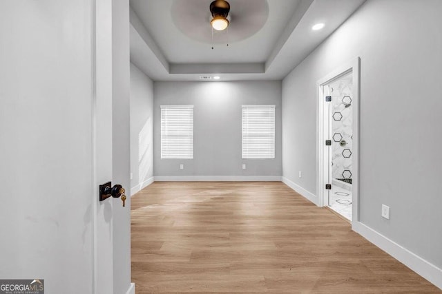 spare room with a tray ceiling, light hardwood / wood-style flooring, and ceiling fan