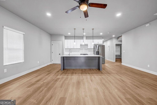 kitchen featuring pendant lighting, white cabinetry, decorative backsplash, a kitchen island with sink, and stainless steel fridge with ice dispenser