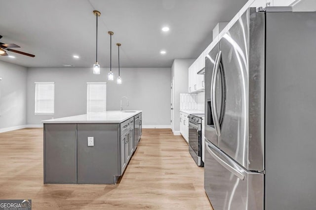 kitchen featuring light hardwood / wood-style flooring, appliances with stainless steel finishes, white cabinetry, hanging light fixtures, and a kitchen island with sink