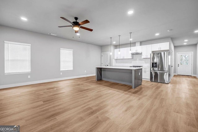 kitchen with a breakfast bar, white cabinetry, decorative light fixtures, a center island with sink, and stainless steel fridge