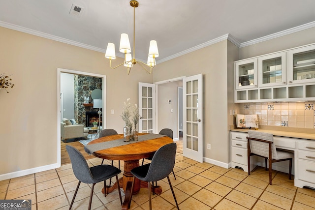 tiled dining area featuring french doors, crown molding, an inviting chandelier, and a stone fireplace