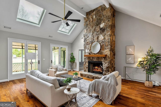 living room featuring wood-type flooring, a skylight, beamed ceiling, ceiling fan, and a fireplace