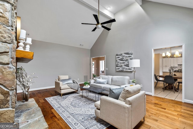 living room with ceiling fan with notable chandelier, high vaulted ceiling, beam ceiling, and light hardwood / wood-style floors