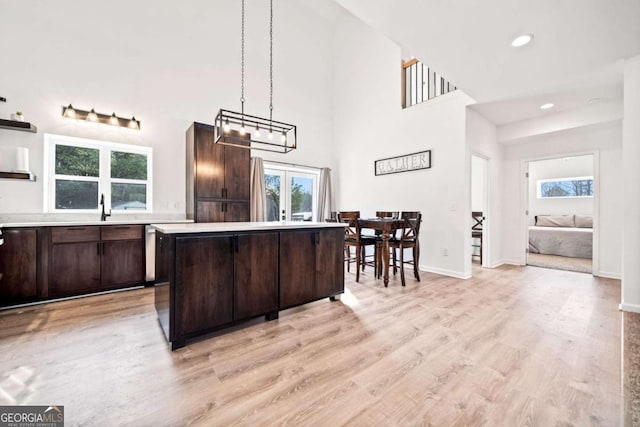 kitchen with hanging light fixtures, a kitchen island, dark brown cabinets, and light hardwood / wood-style flooring