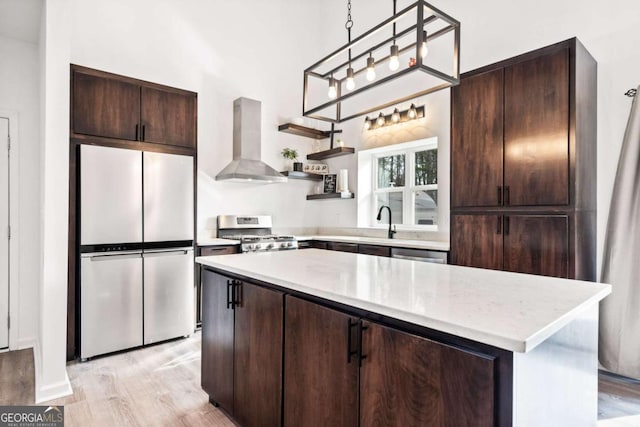 kitchen featuring appliances with stainless steel finishes, ventilation hood, a center island, light hardwood / wood-style floors, and dark brown cabinets