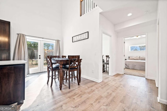 dining area with a wealth of natural light, light hardwood / wood-style flooring, french doors, and a high ceiling