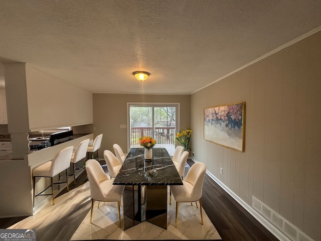 dining space featuring light hardwood / wood-style flooring, ornamental molding, and a textured ceiling