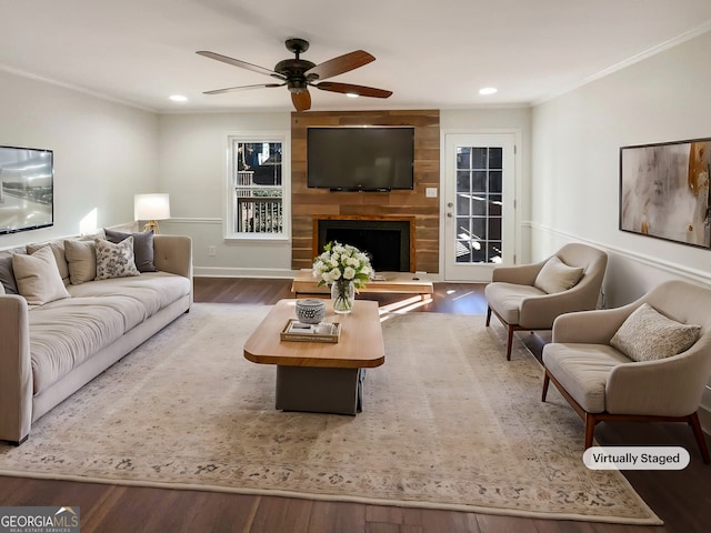 living room featuring wood-type flooring, ornamental molding, a large fireplace, and ceiling fan