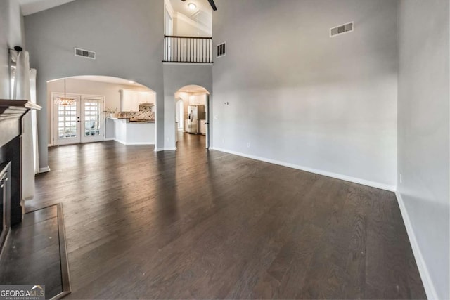 unfurnished living room with dark hardwood / wood-style flooring, a towering ceiling, and french doors