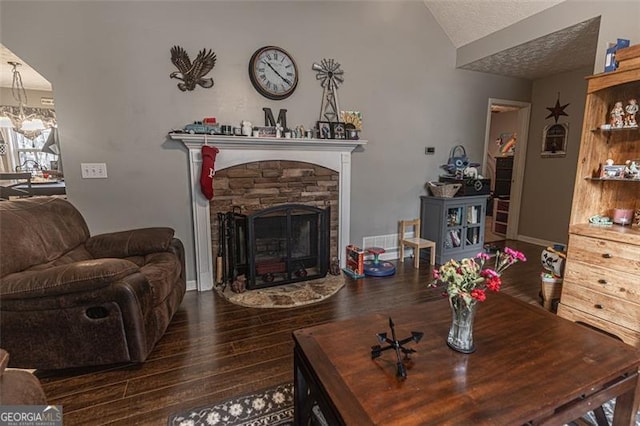 living room with dark hardwood / wood-style flooring, a stone fireplace, a textured ceiling, and an inviting chandelier