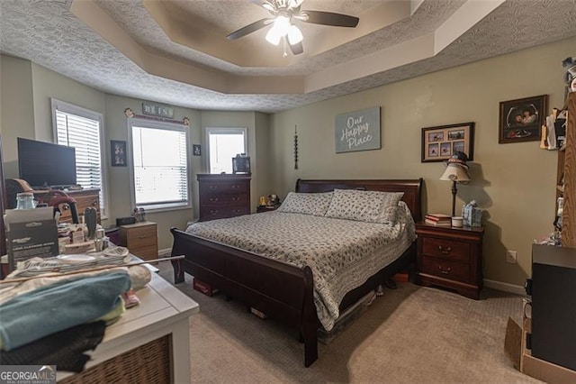 bedroom with ceiling fan, a tray ceiling, light colored carpet, and a textured ceiling