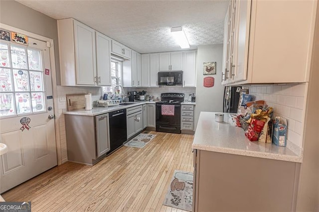 kitchen with sink, backsplash, light wood-type flooring, and black appliances