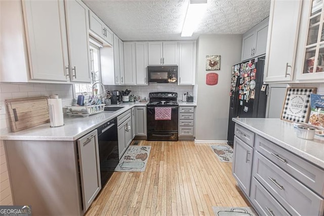 kitchen featuring gray cabinetry, sink, light hardwood / wood-style flooring, and black appliances