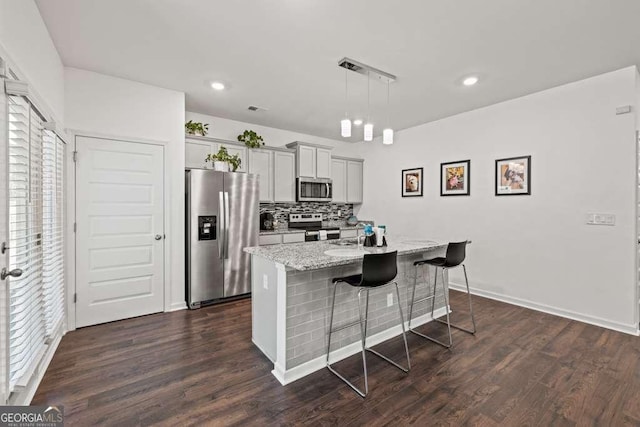 kitchen featuring a breakfast bar area, gray cabinetry, a kitchen island with sink, light stone counters, and stainless steel appliances