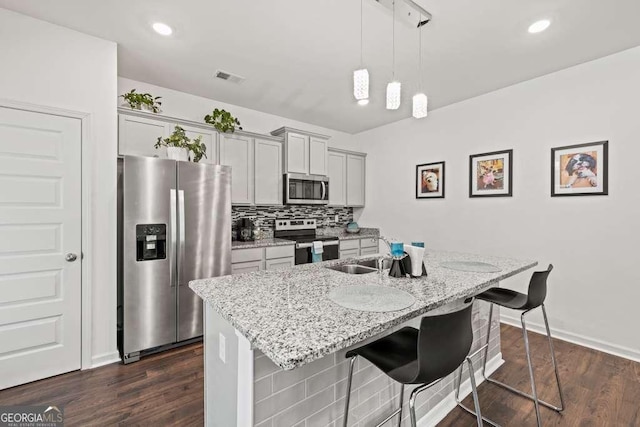 kitchen featuring appliances with stainless steel finishes, gray cabinetry, a kitchen breakfast bar, a kitchen island with sink, and light stone counters