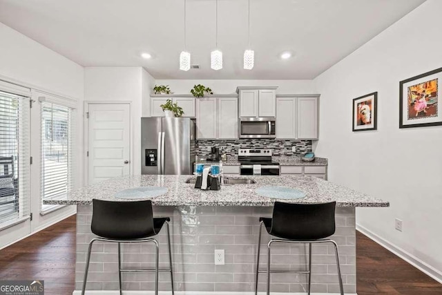 kitchen with a breakfast bar, light stone counters, stainless steel appliances, a kitchen island with sink, and decorative backsplash