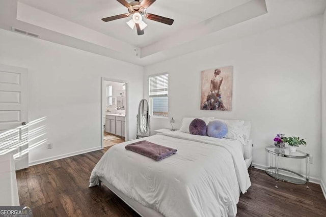 bedroom featuring dark wood-type flooring, ceiling fan, connected bathroom, and a tray ceiling