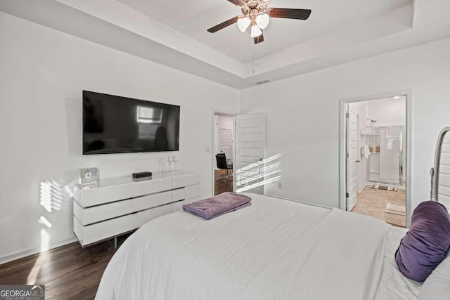 bedroom featuring ceiling fan, a tray ceiling, dark hardwood / wood-style flooring, and ensuite bath