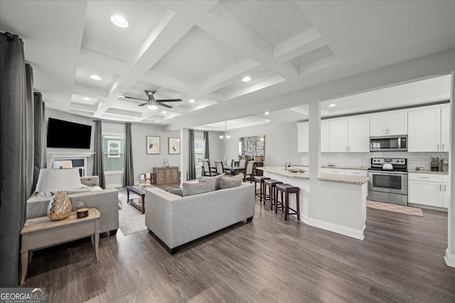 living room featuring coffered ceiling, ceiling fan with notable chandelier, dark wood-type flooring, and beamed ceiling