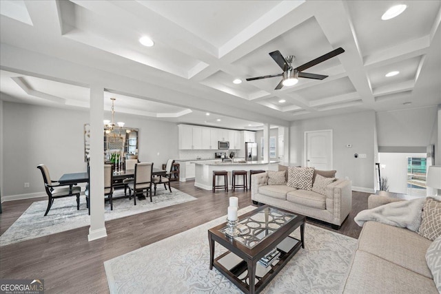 living room featuring hardwood / wood-style flooring, coffered ceiling, ceiling fan with notable chandelier, and beam ceiling